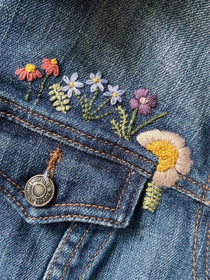 the back pocket of a jean jacket with flowers embroidered on it and a coin in the pocket