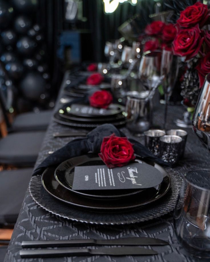 the table is set with black and silver plates, napkins, and red roses