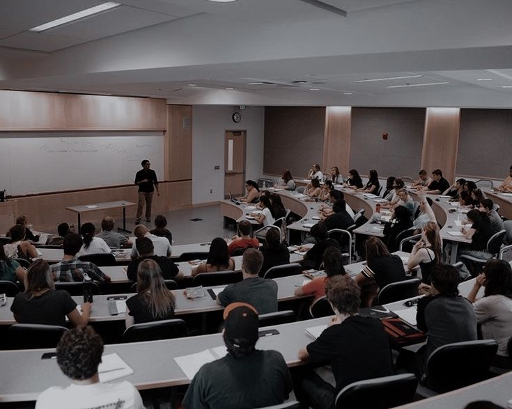 a class room full of people sitting at desks and listening to someone on the screen