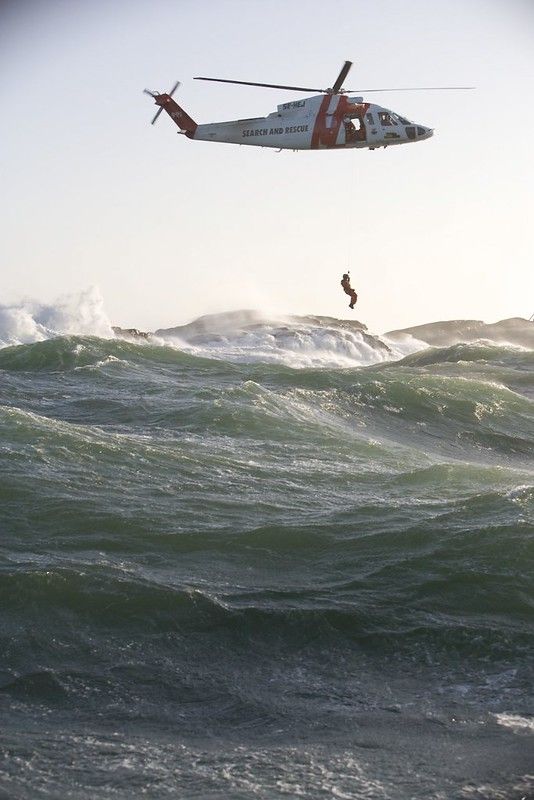 a helicopter flying over the ocean with a person on a surfboard in front of it