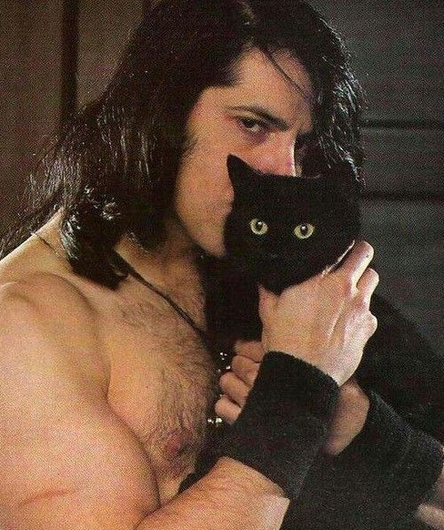 a shirtless man holding a black cat