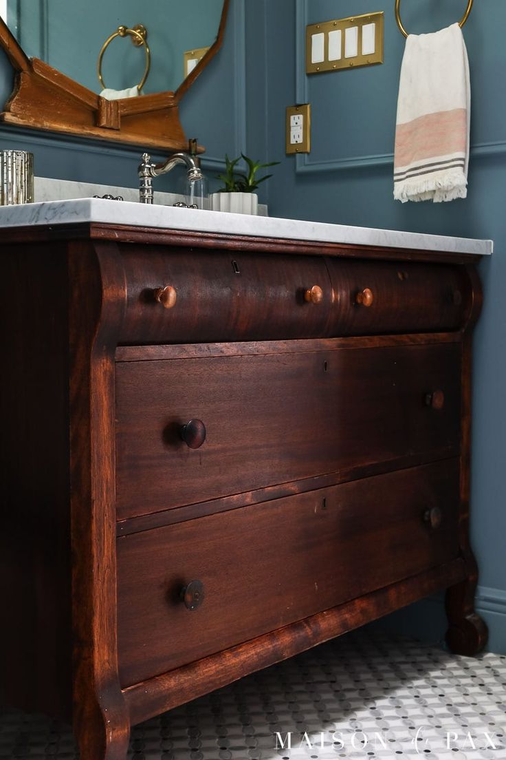 a bathroom with blue walls and a wooden dresser next to a white counter top under a mirror