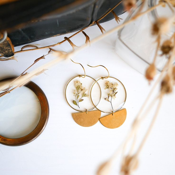 Our best selling Phase Earrings finished with the Meadow Collection Botanicals. These earrings are big and bold but super lightweight, making them the perfect statement earring for all day wear. The monochromatic look makes them easy to wear with any outfit! The Meadow is know to symbolize growth, renewal, and the cycles of life. Ear hooks are gold plated over brass and hypoallergenic. Ships in gift worthy packaging. The symbolism of the botanical is printed on a tag included with your jewelry. Nature Inspired Earrings, Elf Maiden, Dried Flower Earrings, Cycles Of Life, Easy Crafts To Sell, Botanical Earrings, Artisan Earrings, Botanical Jewelry, Statement Earring