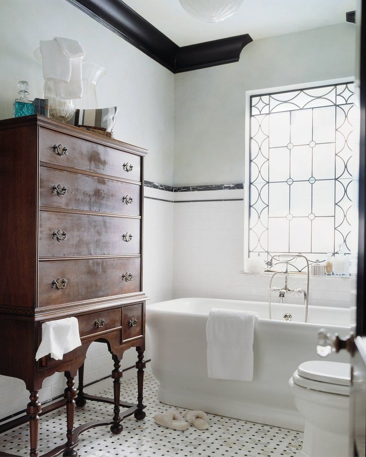 a white bathroom with black and white flooring, an old dresser, and a bathtub