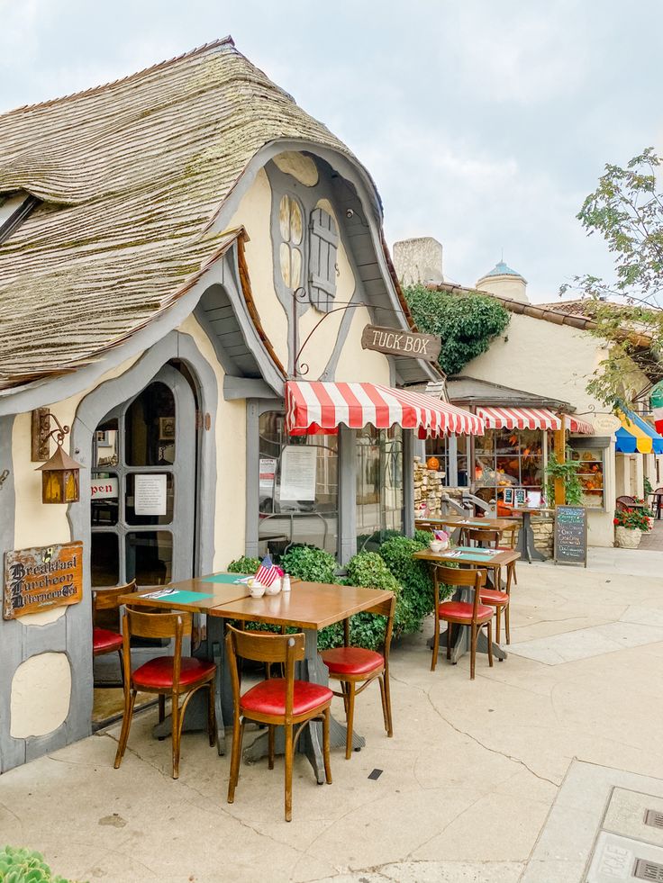 an outdoor cafe with red chairs and tables in front of the building that is shaped like a house