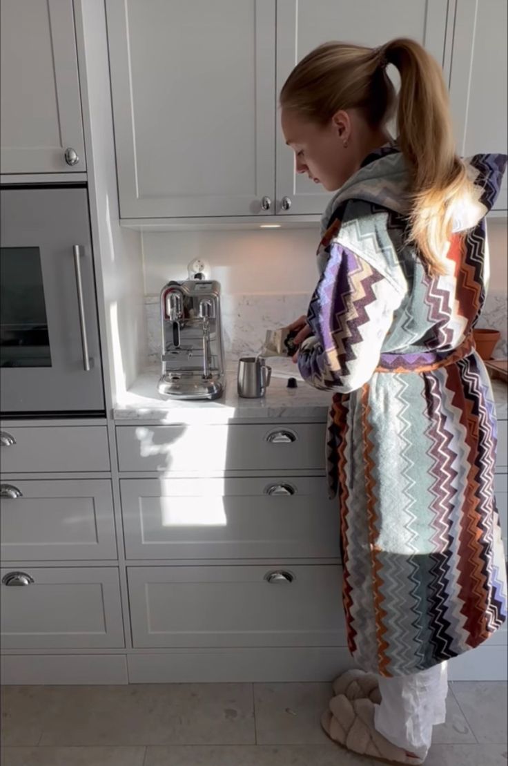 a woman standing in front of a kitchen counter next to a stove top oven and microwave