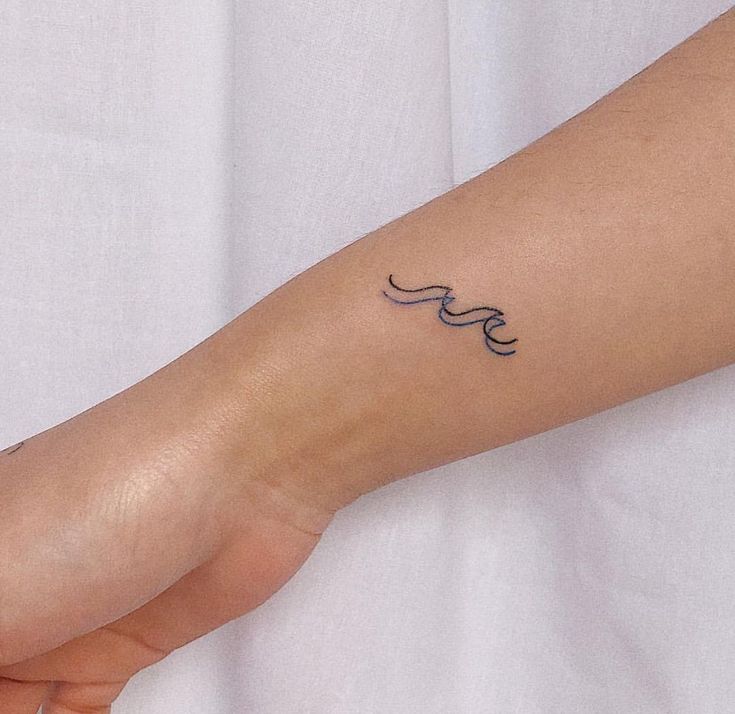 a woman's arm with a wave tattoo on the left side of her wrist