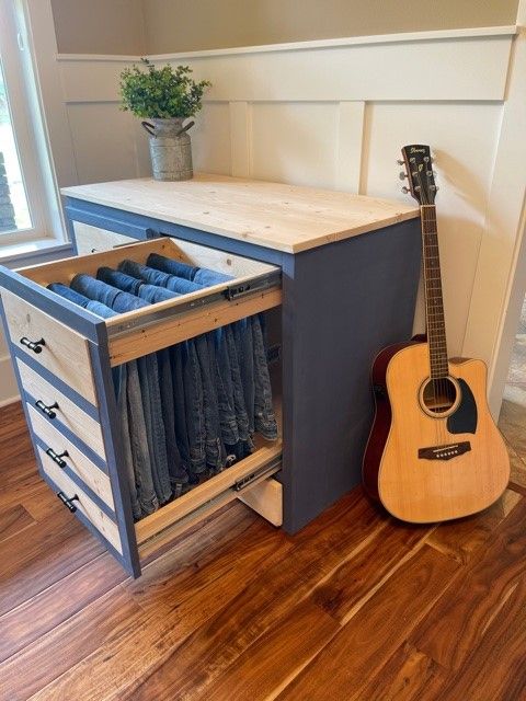 a guitar is sitting on the floor next to an open drawer with jeans in it