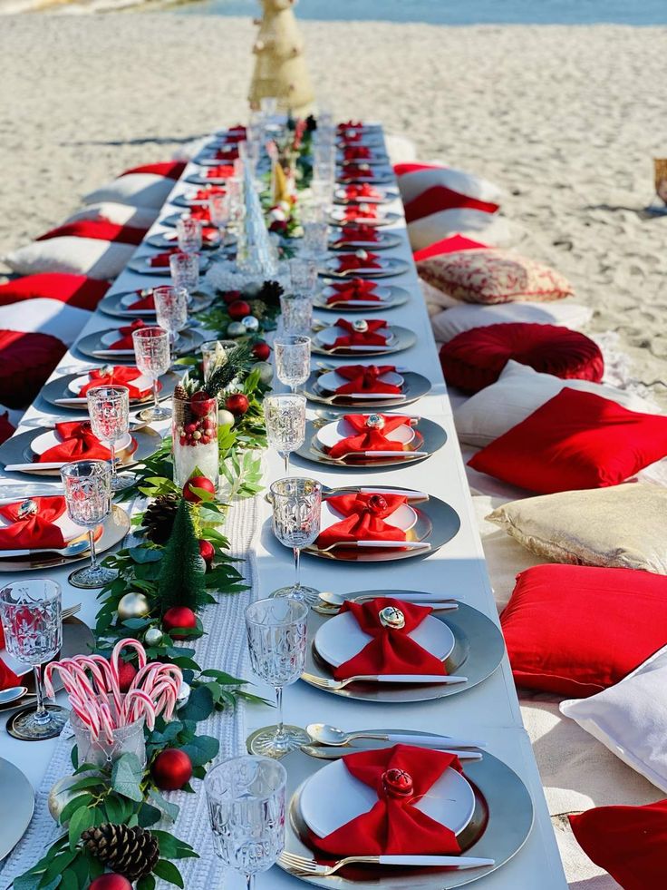 a long table is set up on the beach for an outdoor christmas party with red and white decorations