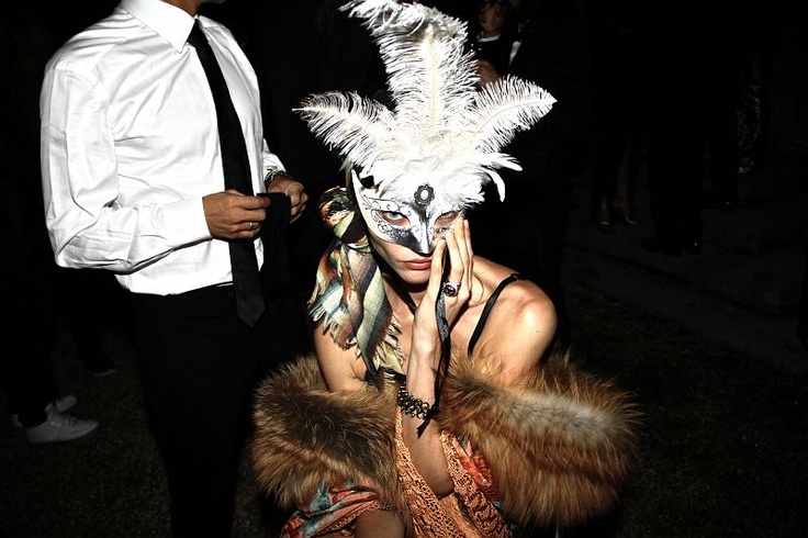 a woman wearing a white mask with feathers on her face at a costume party in the dark