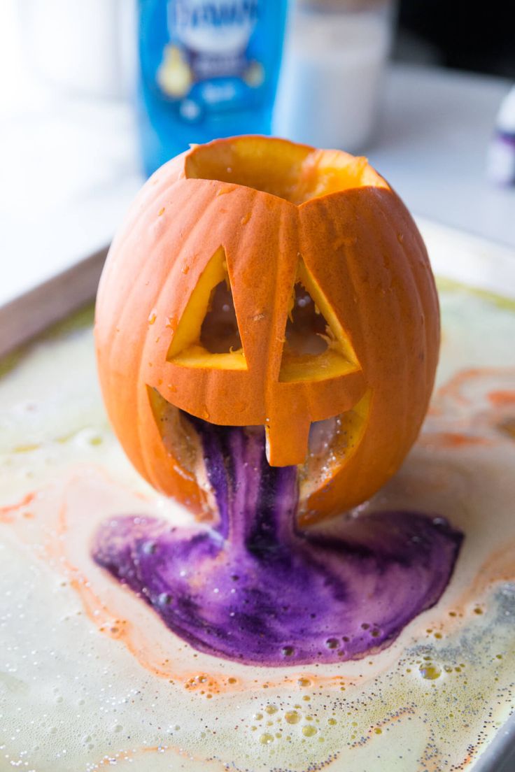 a halloween pumpkin with purple liquid pouring out of it's mouth on a baking sheet