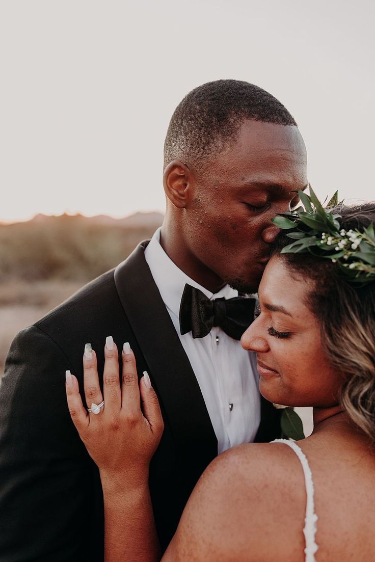 a bride and groom embracing each other in front of the sun at their desert wedding