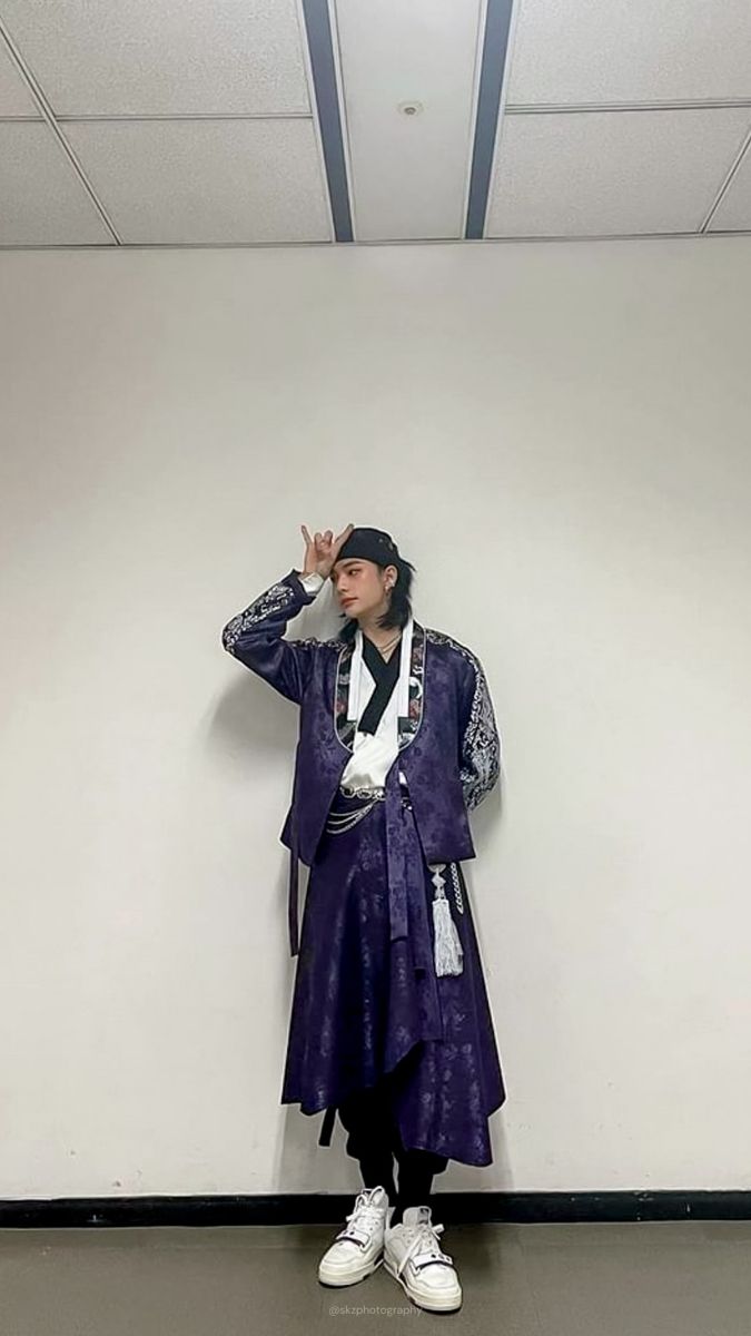 a person standing in front of a white wall wearing a purple coat and hat with his hand on his head