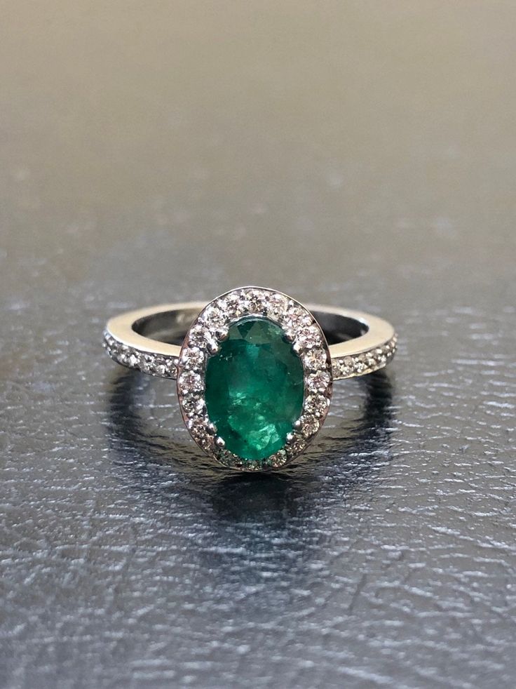 an emerald and diamond halo ring on a black surface with white diamonds around the band