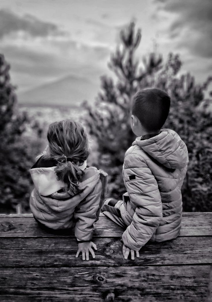 two children sitting on a bench looking at the trees