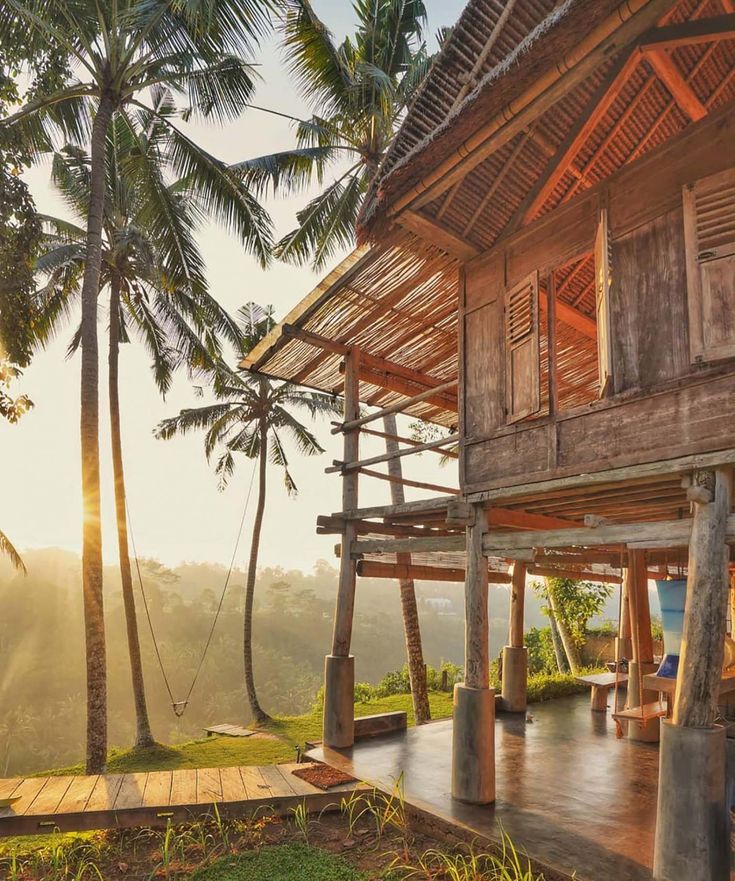 a wooden house sitting on top of a lush green hillside next to tall palm trees