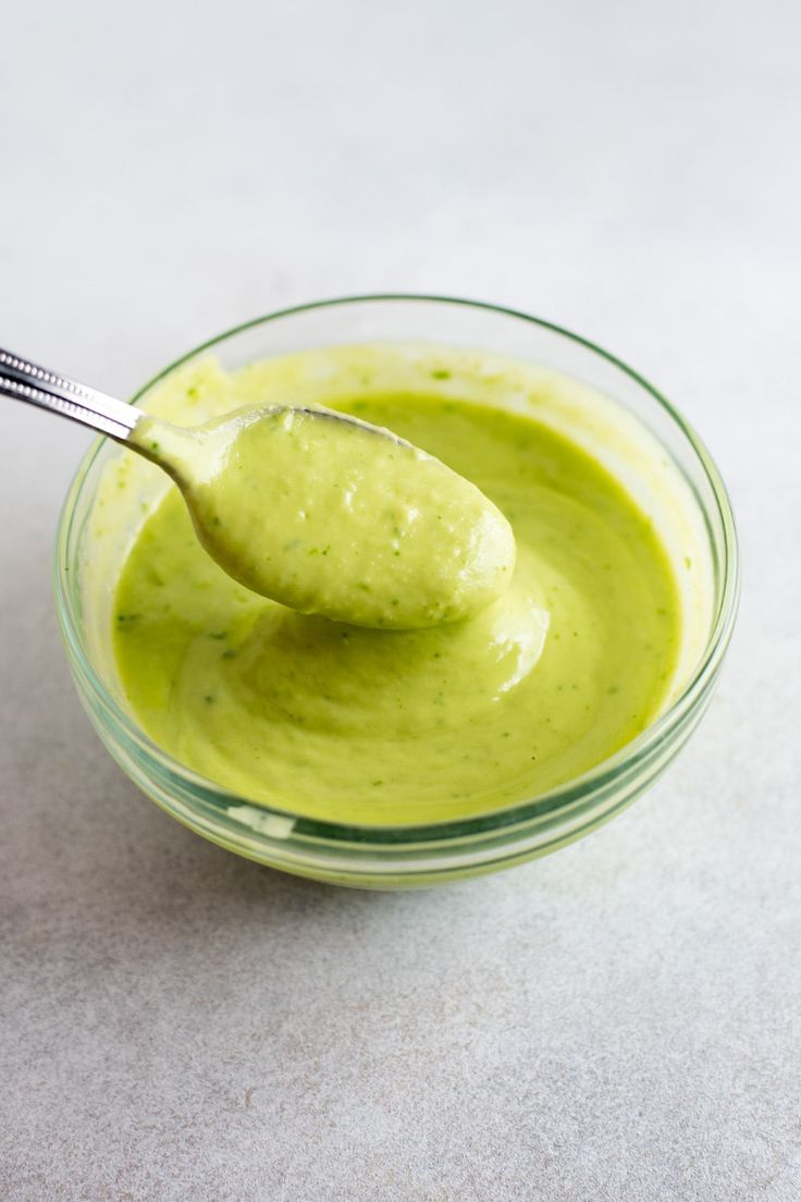 a spoon full of green sauce in a glass bowl