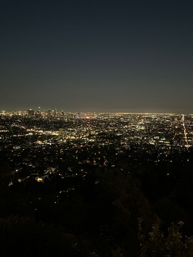 the city lights are lit up at night in this view from an overlook point on top of a hill