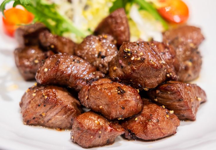 meat and vegetables on a white plate with lettuce, tomato and salad in the background