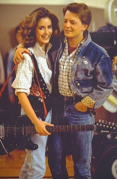 a man and woman standing next to each other holding an electric guitar in their hands