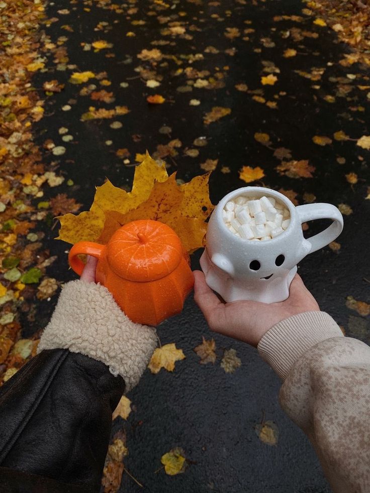 a person holding a coffee cup with marshmallows in it and an orange pumpkin