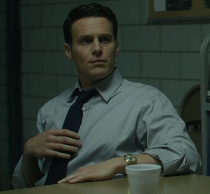 a man sitting at a table with a coffee cup in his hand and wearing a tie