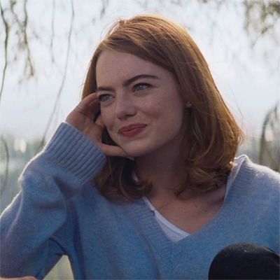 a woman with red hair wearing a blue sweater and talking on a cell phone in front of a tree