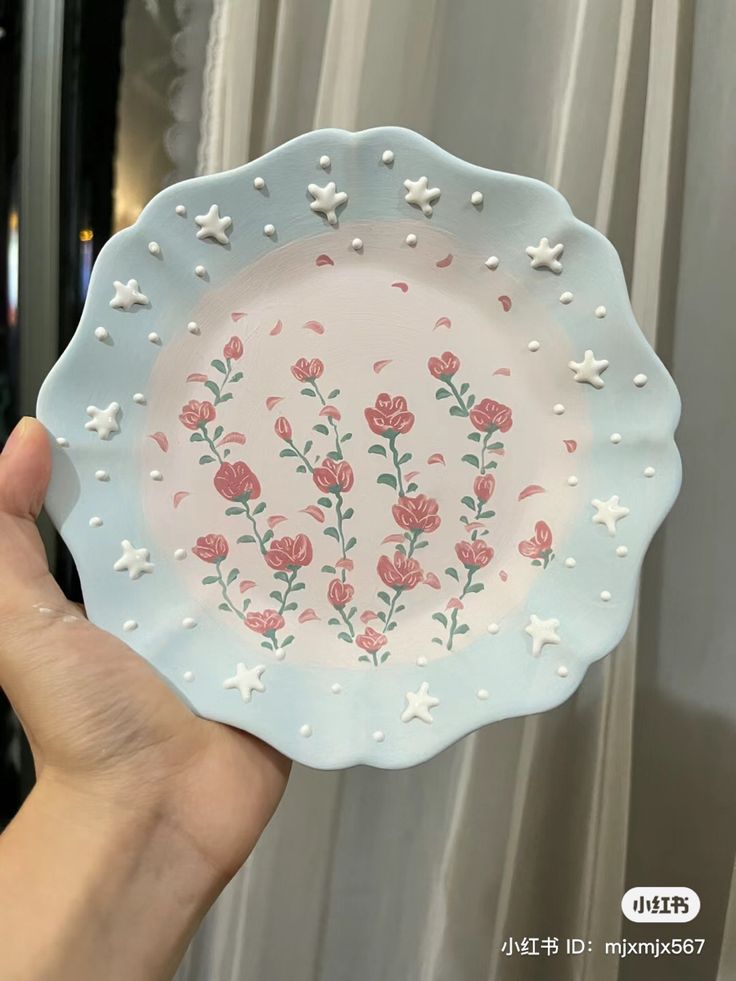 a hand holding a plate with flowers painted on it