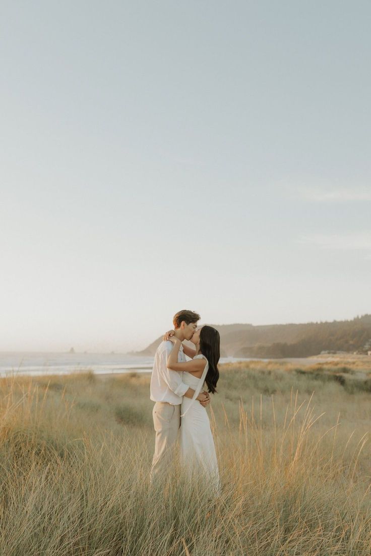 a couple kissing in tall grass by the ocean