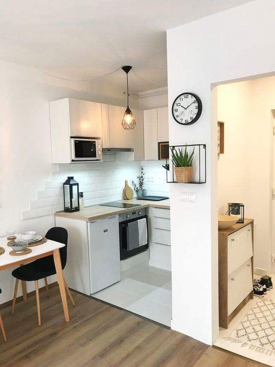 a kitchen with white walls and wooden floors has a clock on the wall above the stove