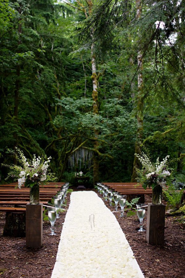 an outdoor wedding ceremony setup with white flowers and greenery on the aisle, surrounded by tall trees