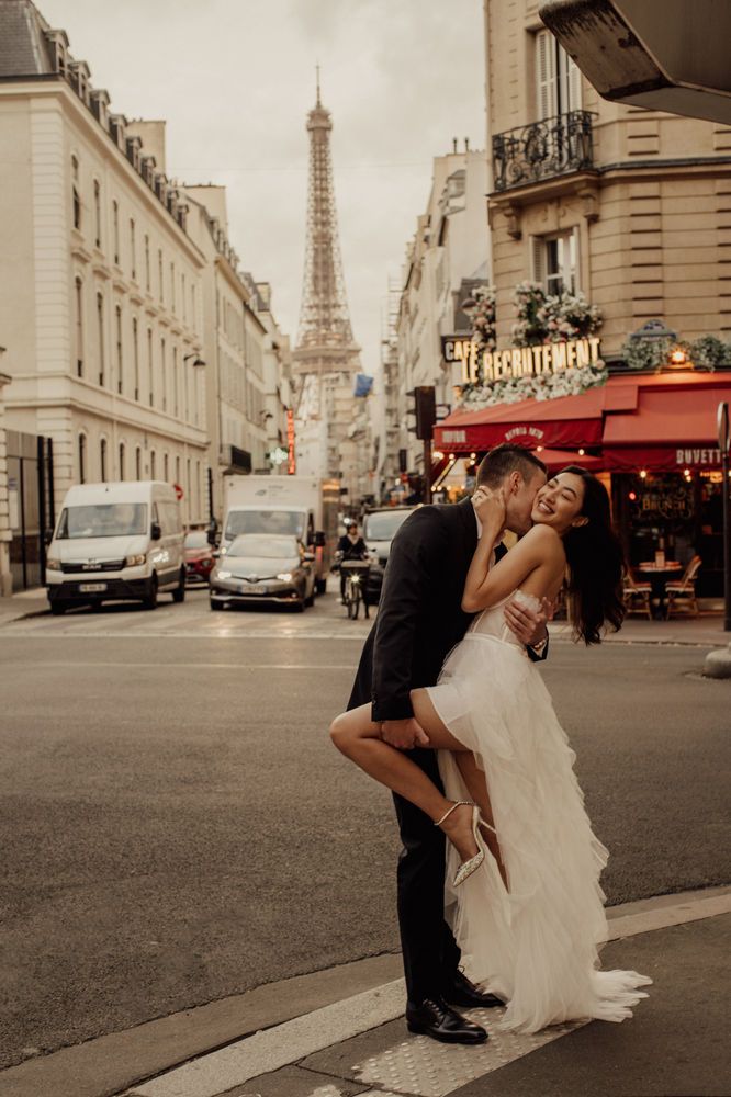 a newly married couple kissing on the street in front of the eiffel tower