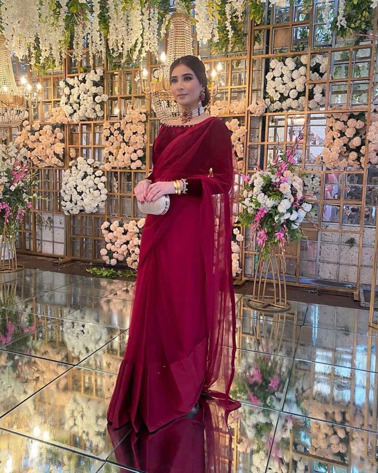 a woman in a red dress standing on a floor with flowers and greenery behind her