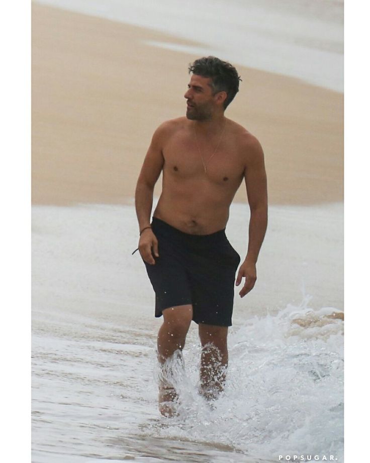 a shirtless man walking in the water at the beach