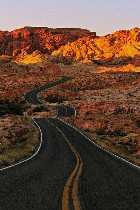 an empty road in the desert with mountains in the backgrounnd and blue sky