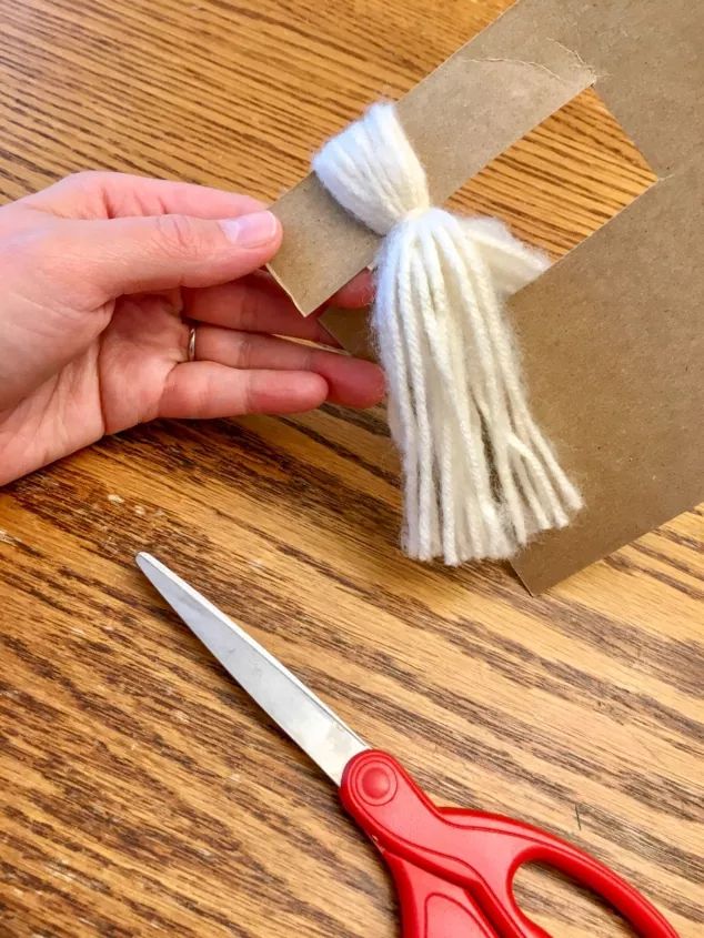 someone is cutting paper with scissors on a wooden table next to a piece of cardboard