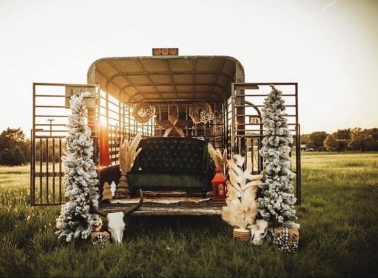 the back end of a horse trailer decorated with christmas trees and garlands, sitting in a grassy field