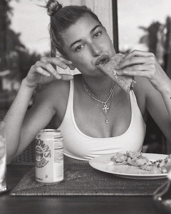 a woman sitting at a table with food in front of her face and eating pizza