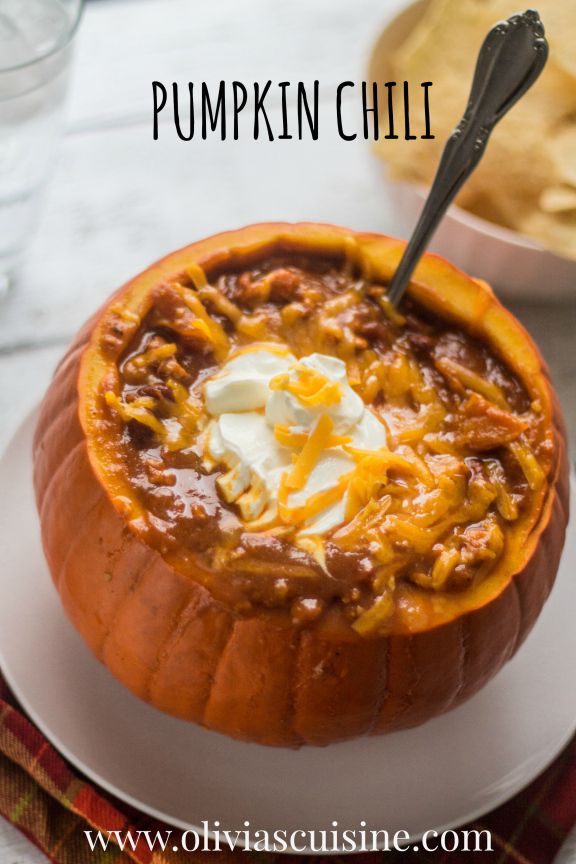 a white plate topped with a pumpkin filled with chili and cheese covered in sour cream