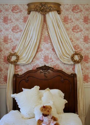 a teddy bear sitting on top of a bed in a room with pink wallpaper