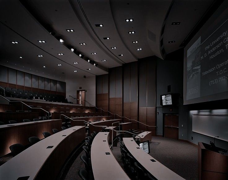 an empty lecture hall with rows of seats and projector screen on the wall in front of it