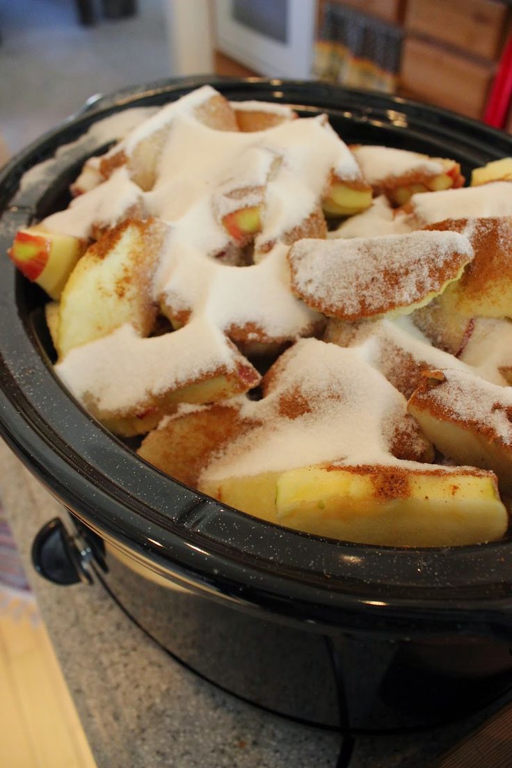 a crock pot filled with powdered sugar and apple slices on top of a counter