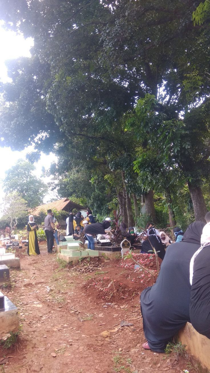 many people are sitting on benches in the woods near some trees and grass, with one person leaning over