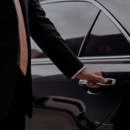 a man in a suit is holding the door handle of a black car with his hand on it