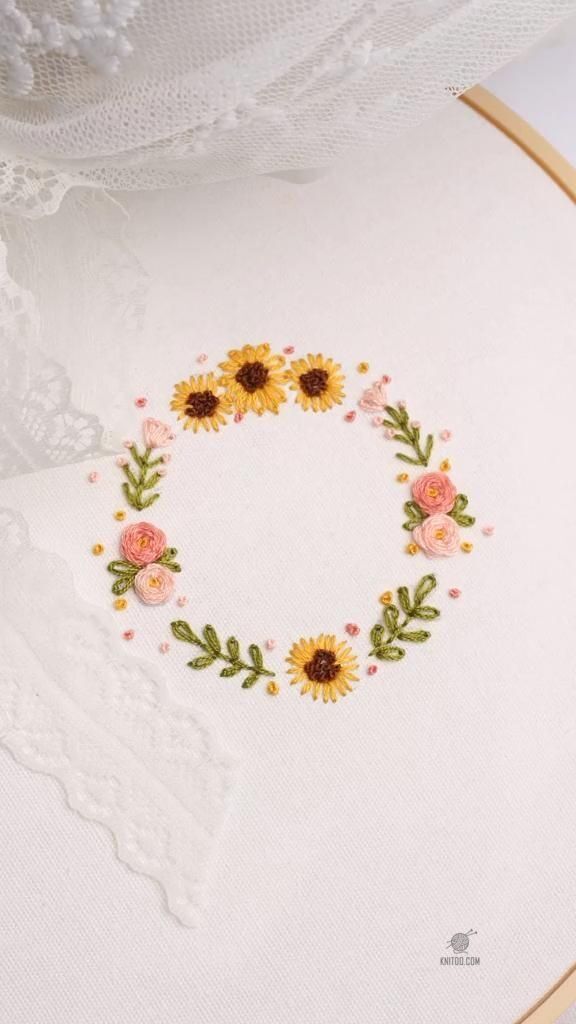 an embroidered sunflower wreath on a white cloth with pink and yellow flowers in the center