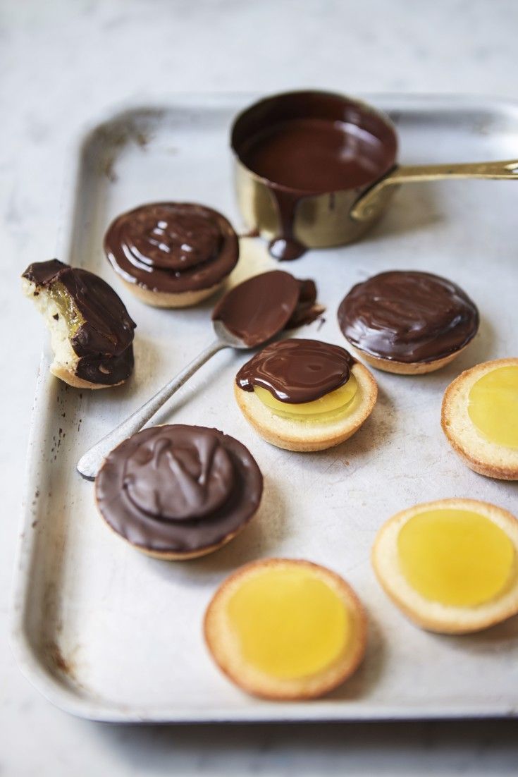 chocolate covered cookies on a baking sheet with spoon and cupcakes in the background