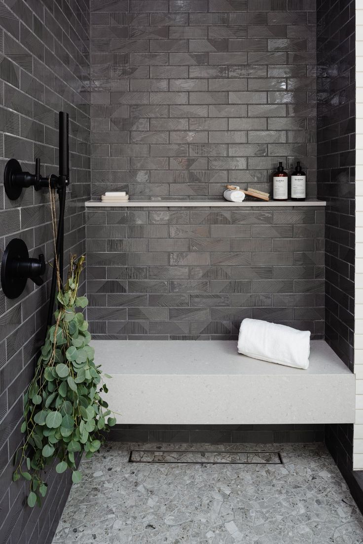 a bathroom with gray brick walls and white counter tops, along with a plant in the corner