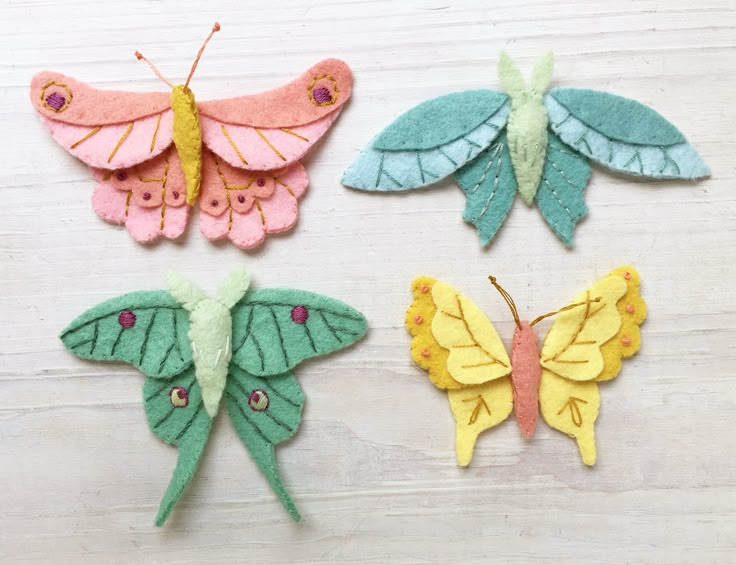 four felt butterflies sitting on top of a wooden table next to each other and one butterfly has its wings folded