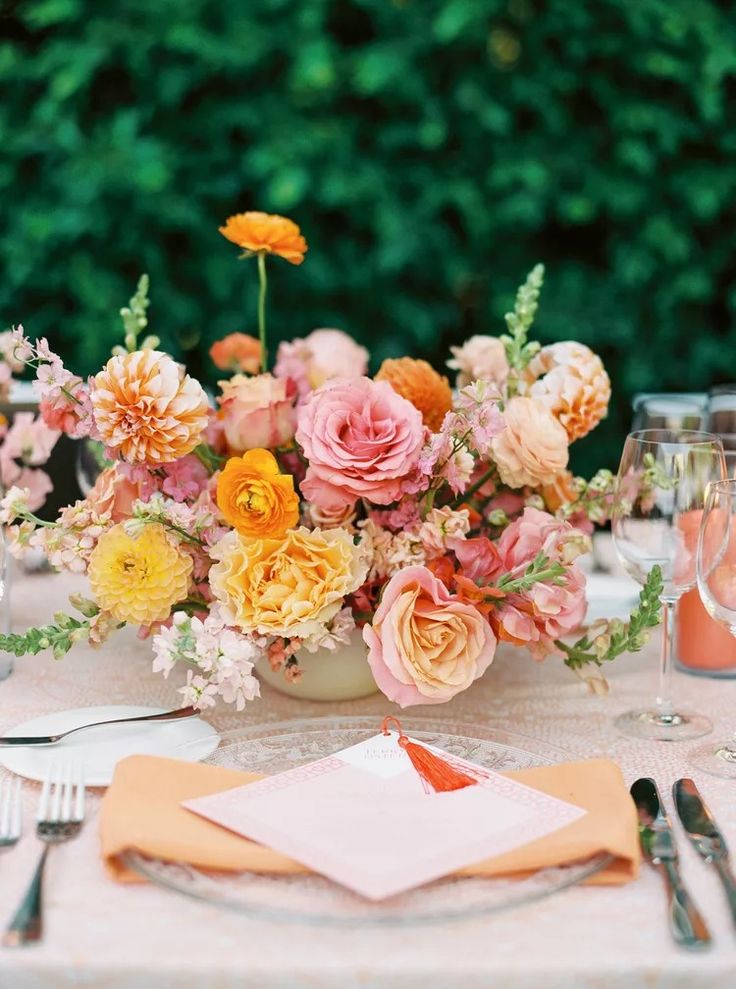 an arrangement of flowers in a vase on a table with silverware and napkins