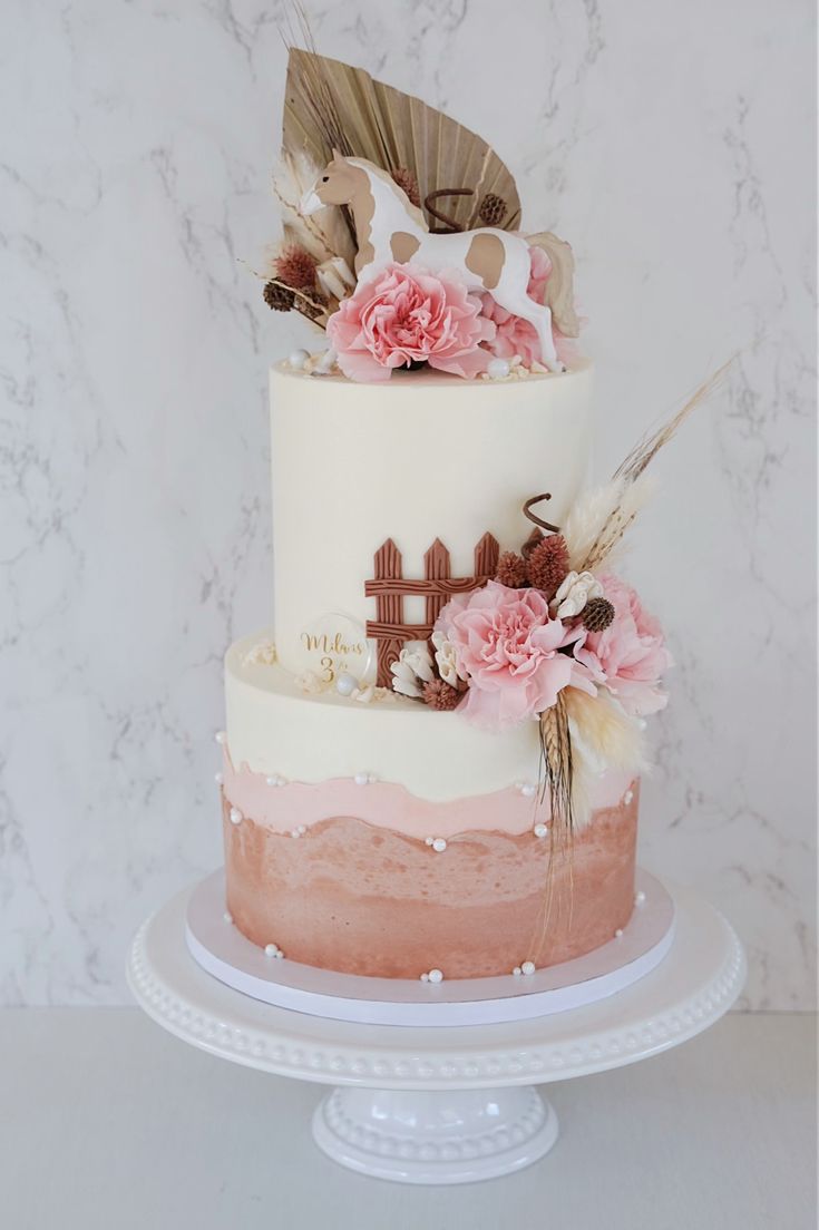 a three tiered cake with pink flowers and feathers on the top is sitting on a plate